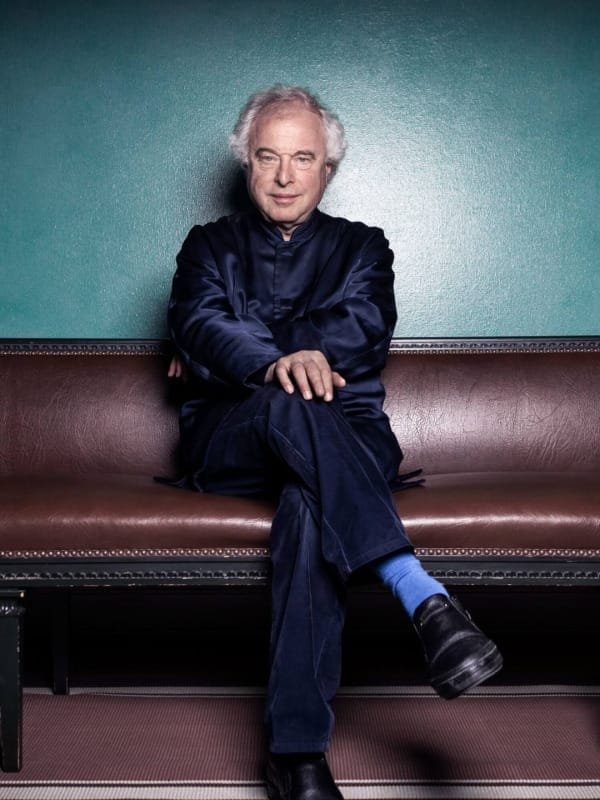 Andras Schiff, a white man in his 70s, is sitting on a sofa.