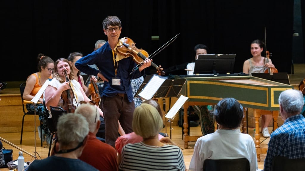 Violinist Matthew Truscott is talking to the audience at an open rehearsal in the Acland Burghley School hall.