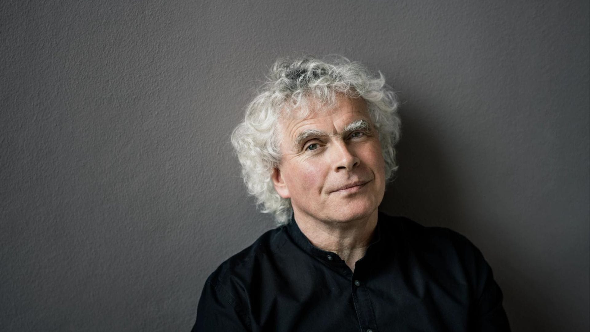 A head-and-shoulders shot of the conductor Simon Rattle, a man with grey curly hair