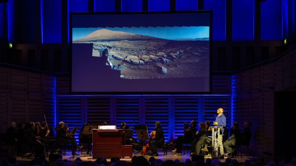 Sanjeev Gupta is giving a talk on a stage - a photo of the surface of Mars is displayed on a large screen.